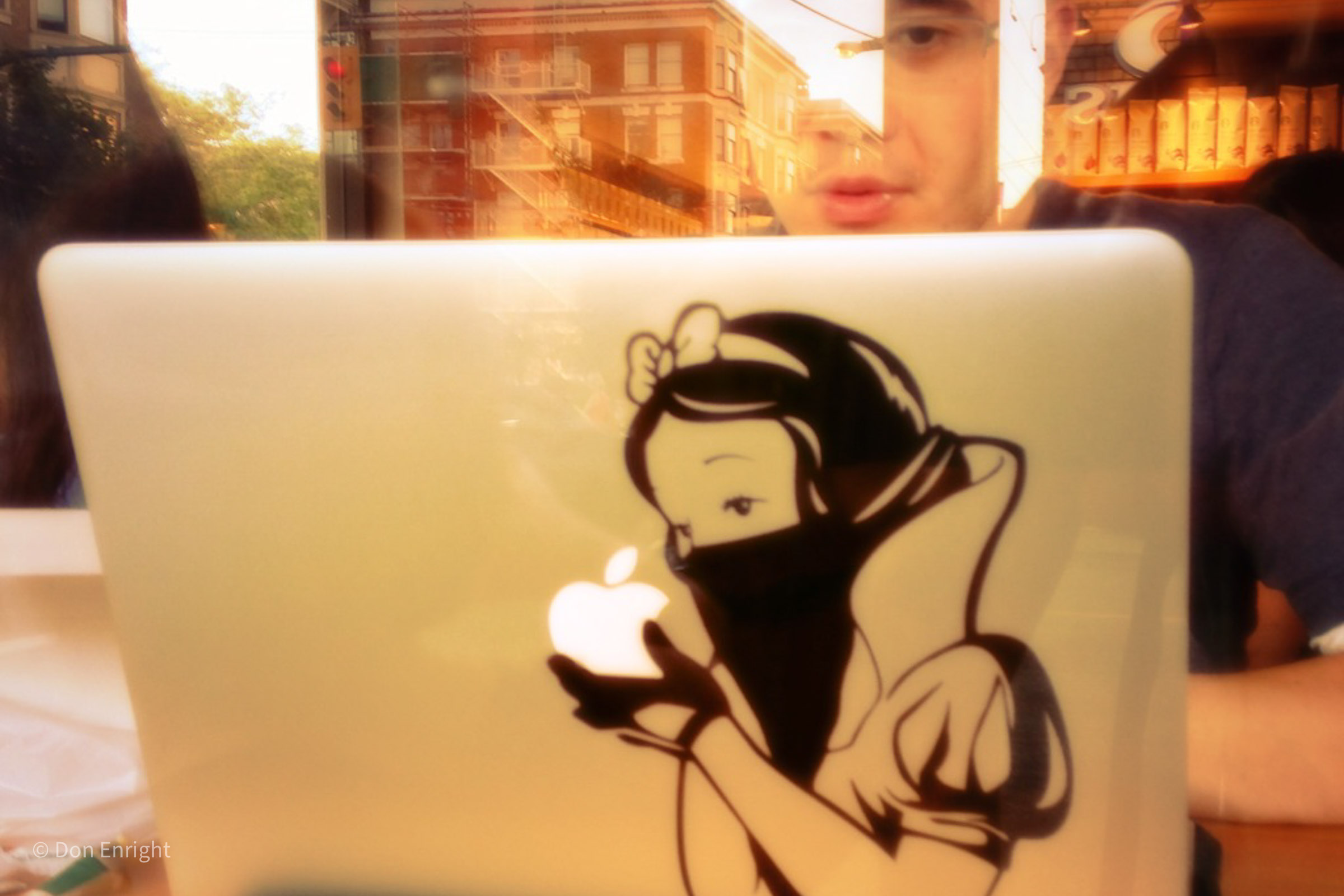 A young man looks at a Mac powerbook that has been customized with a hip decal.